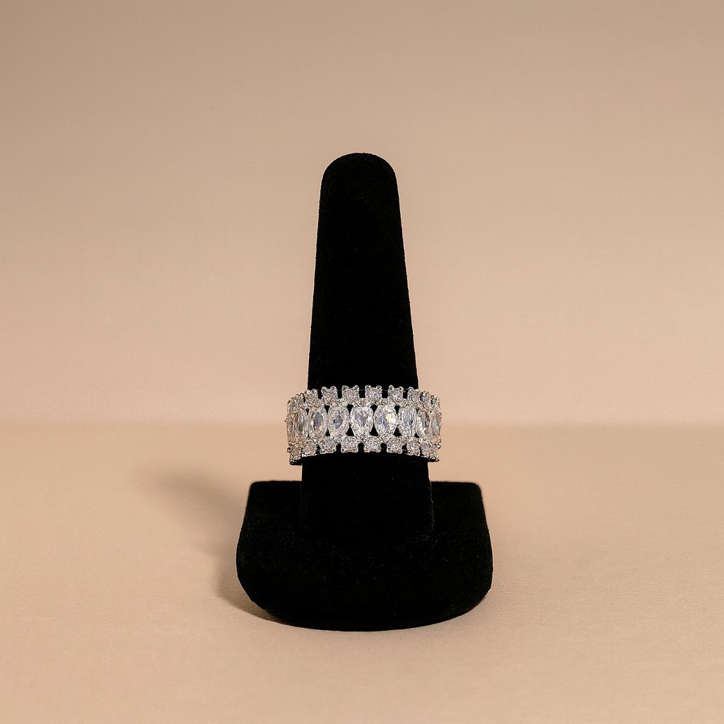 Silver ring with gemstones on a black stand against a beige background